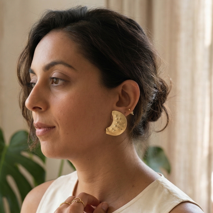 Woman wearing gold earrings and a ring, with a neutral background