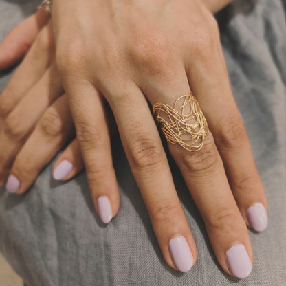 Hand wearing a gold ring with pink nail polish on a neutral background