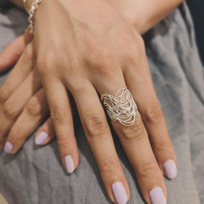 A hand wearing a silver-colored wrap-around ring with multiple bands, displayed on a soft background.
