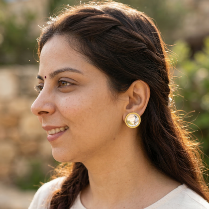 Woman wearing gold earrings with a blurred natural background