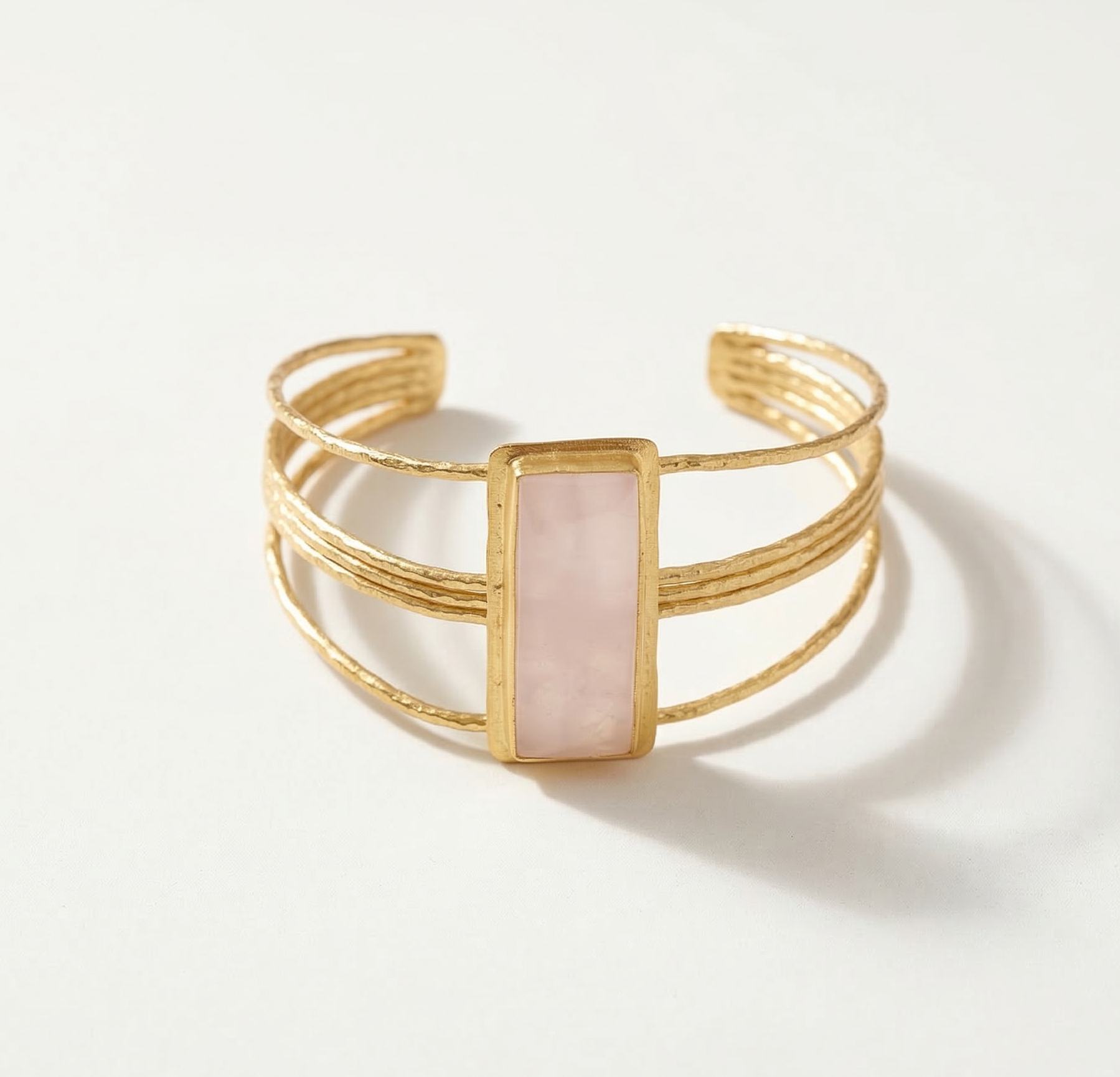Gold bracelet with a pink rose quartz stone on a white background