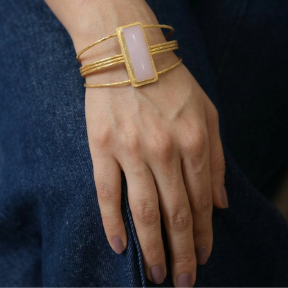 Gold bracelet with a pink stone on a wrist against a dark background
