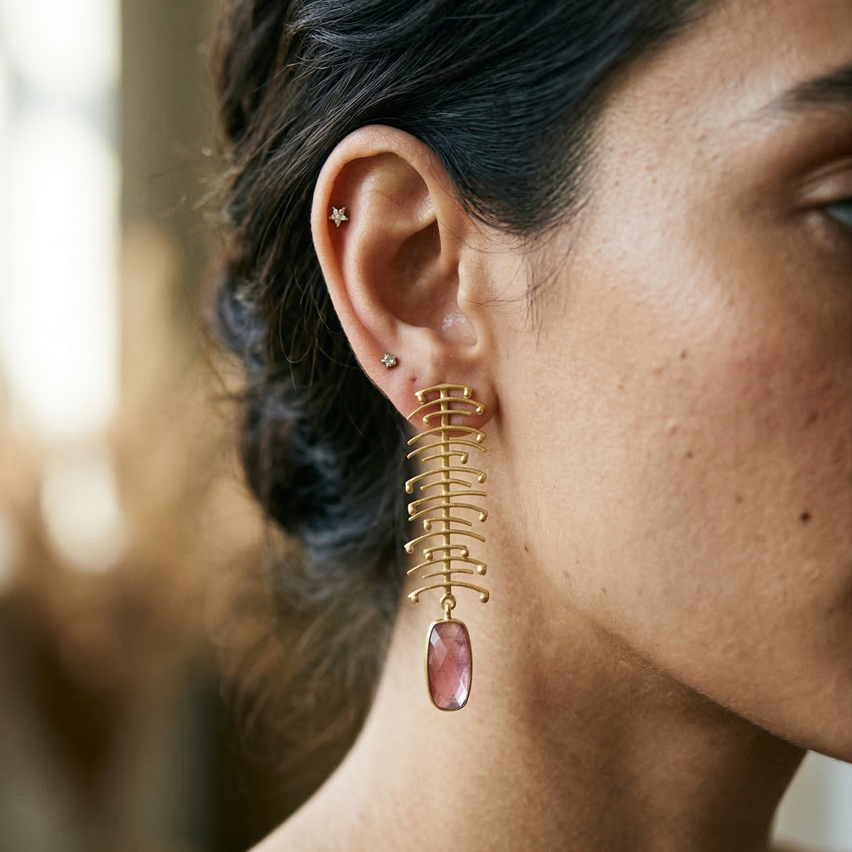 Close-up of a person wearing a gold earring with a pink monalisa gemstone.