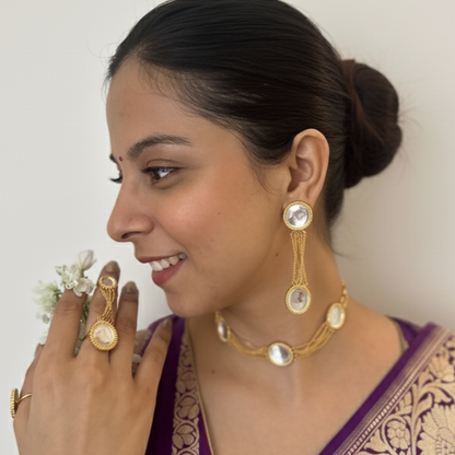 Woman wearing a purple saree with gold jewelry against a white background
