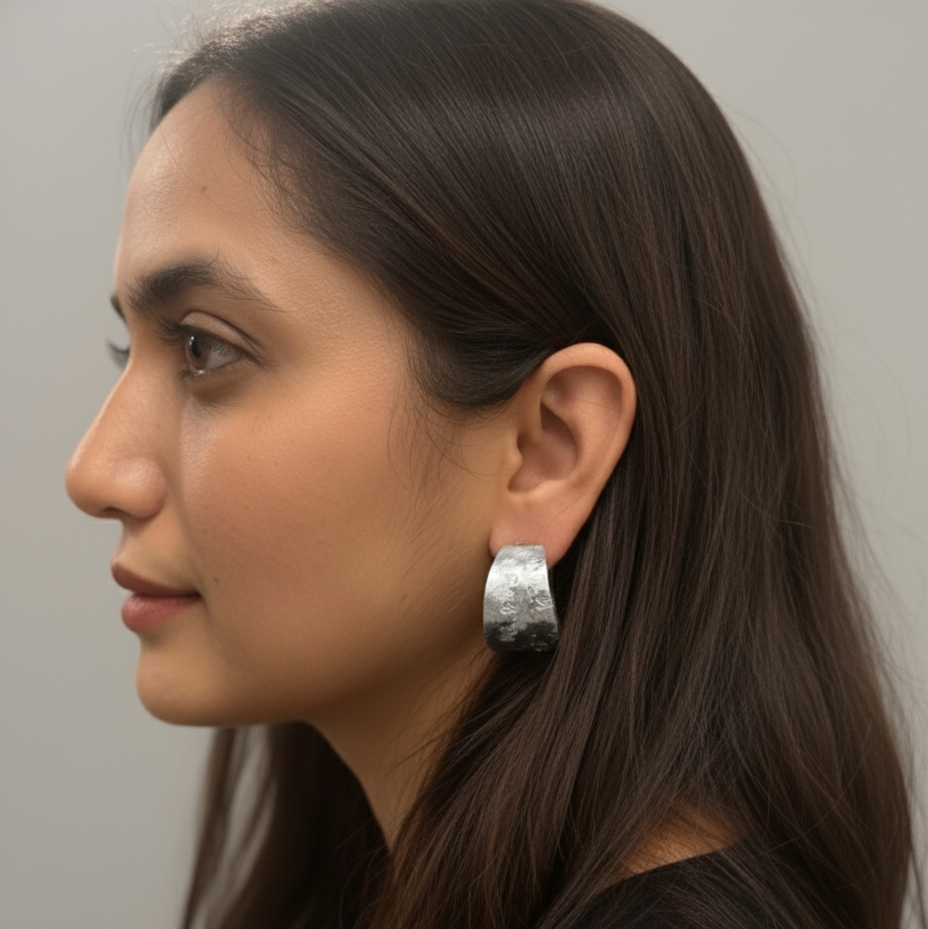 Woman wearing a silver chunky molten textured hoop earring against a plain background