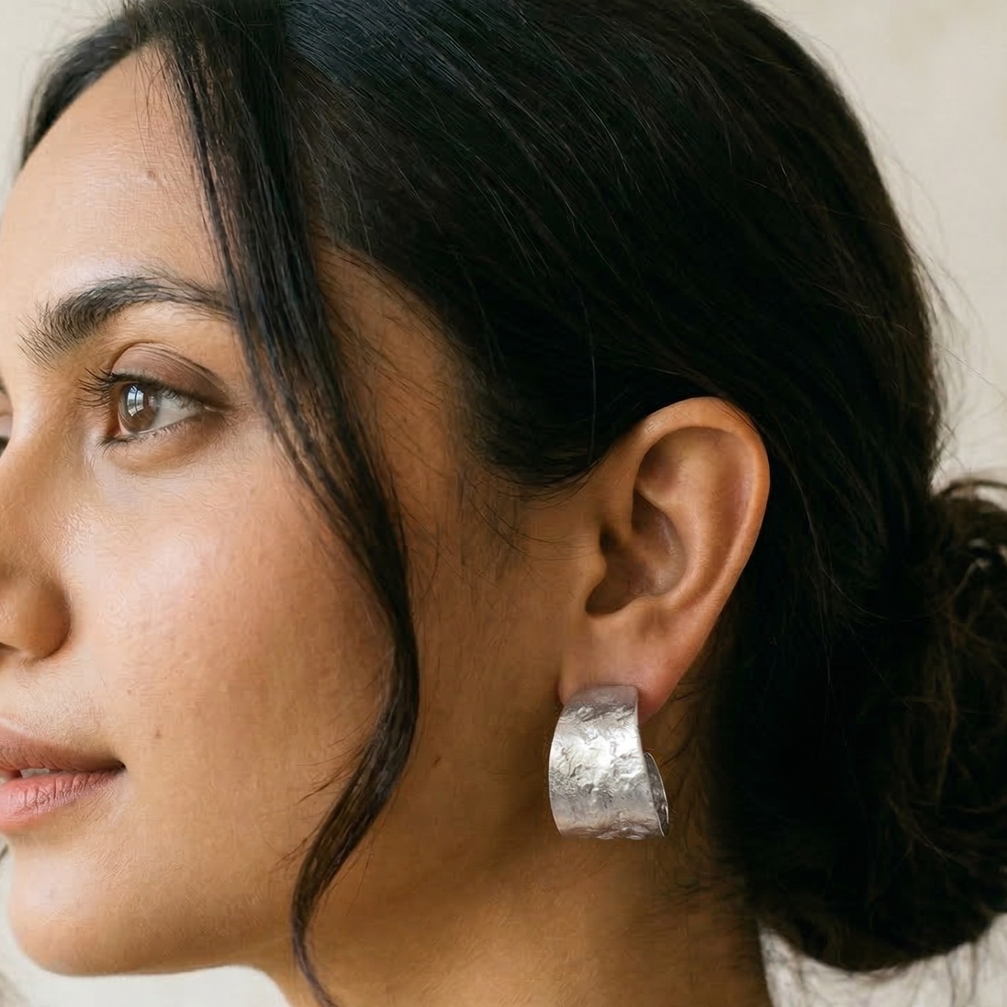 Woman wearing silver hoop earrings with a neutral background