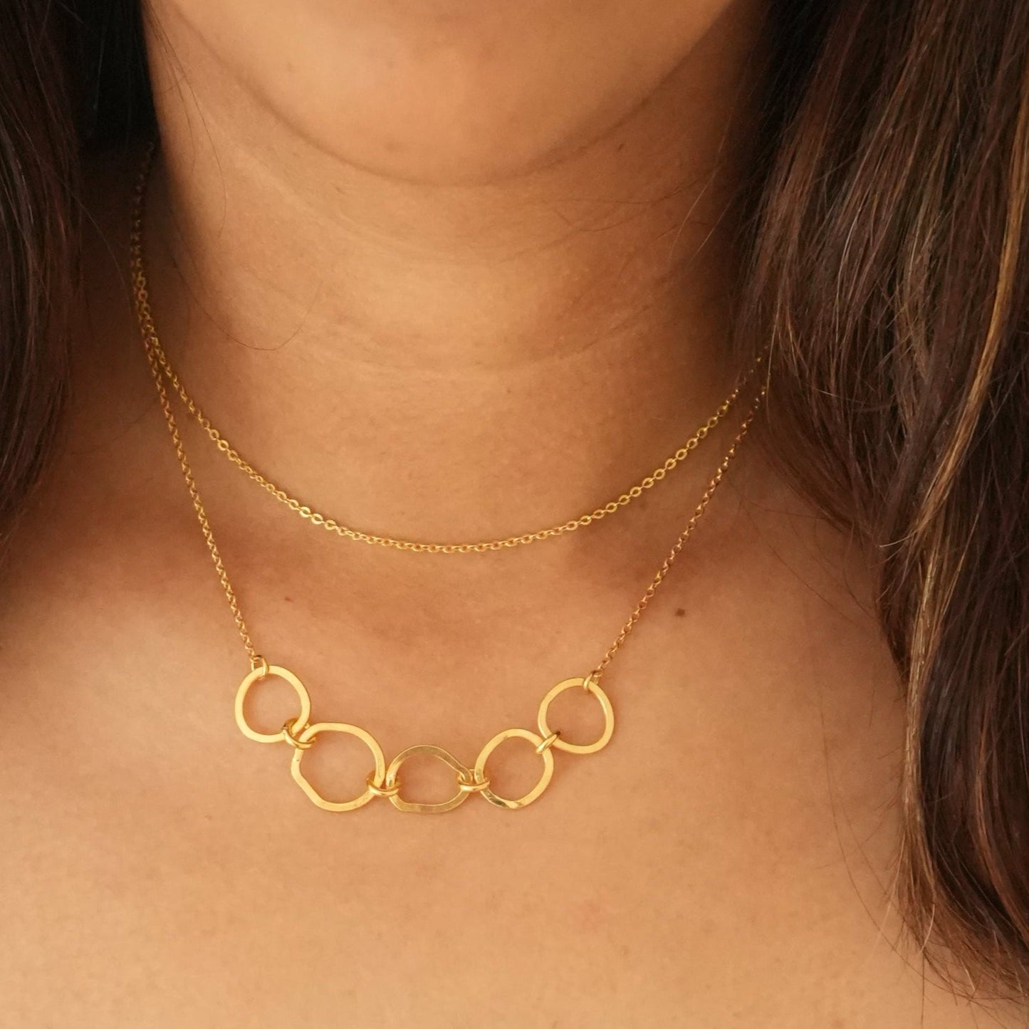 A person wearing a gold-plated necklace with sterling silver and a chain length of 18 inches, layered with another necklace.