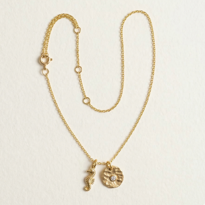 Gold necklace with two charms on a light beige background