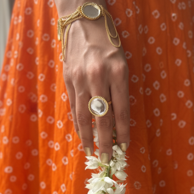 Person wearing an orange traditional outfit with a gold bracelet and ring, holding a white flower garland.