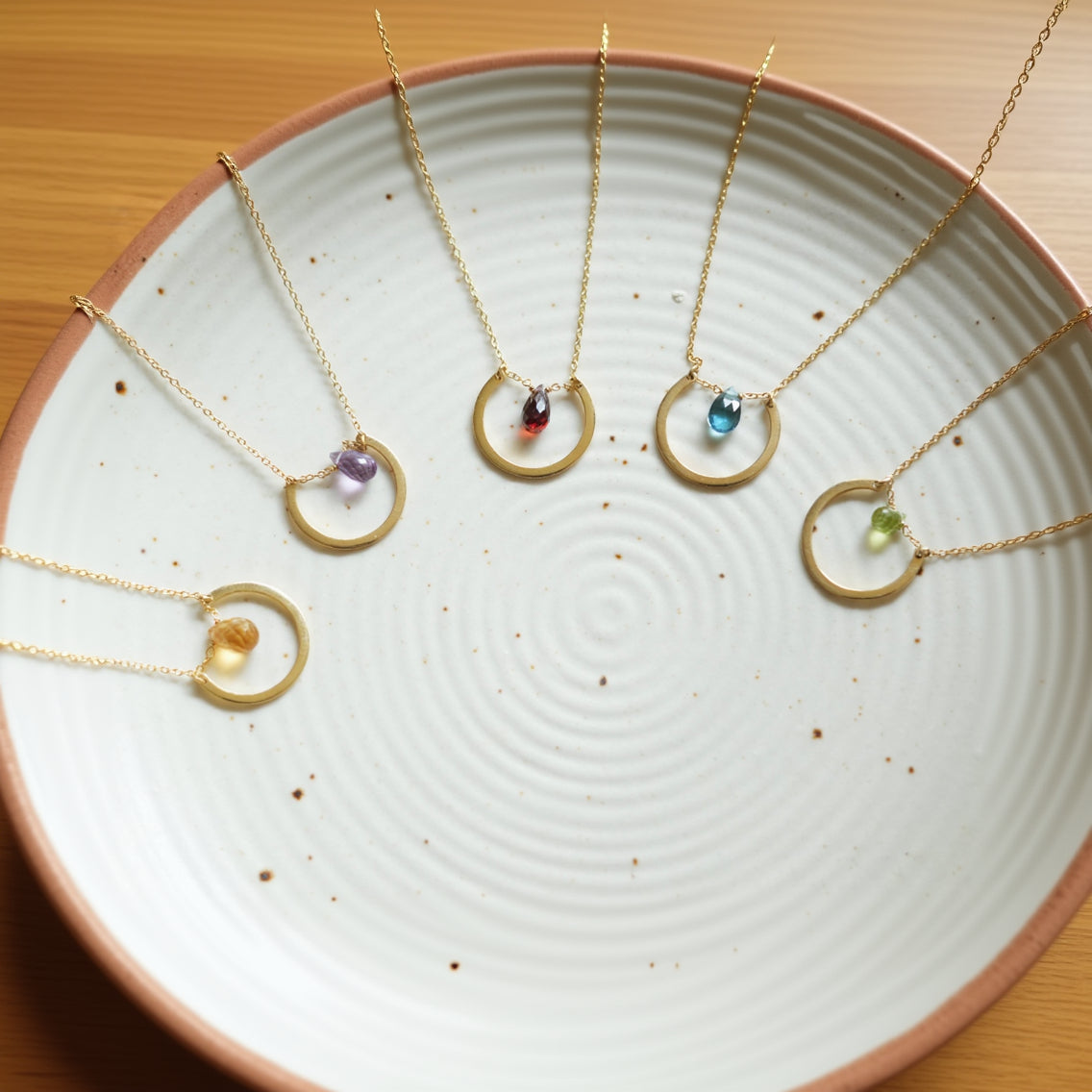 A sterling silver necklace with gold plating, featuring a series of round drop-shaped pendants adorned with various colored semi-precious stones.