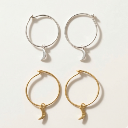 Set of gold and silver hoop earrings with moon charms on a light background