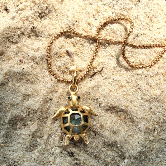 Gold turtle labradorite stone pendant necklace on a sandy surface with shells and pearls