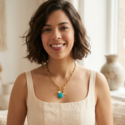 Woman wearing a gold necklace with a turquoise pendant indoors