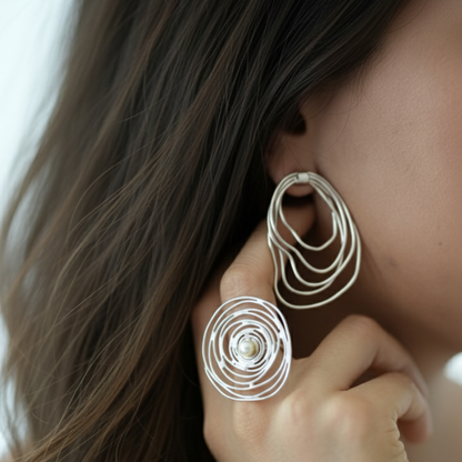 Close-up of a person wearing silver spiral earrings with a pearl center.