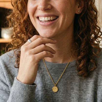 Woman with curly hair wearing a gray sweater and gold necklace indoors.