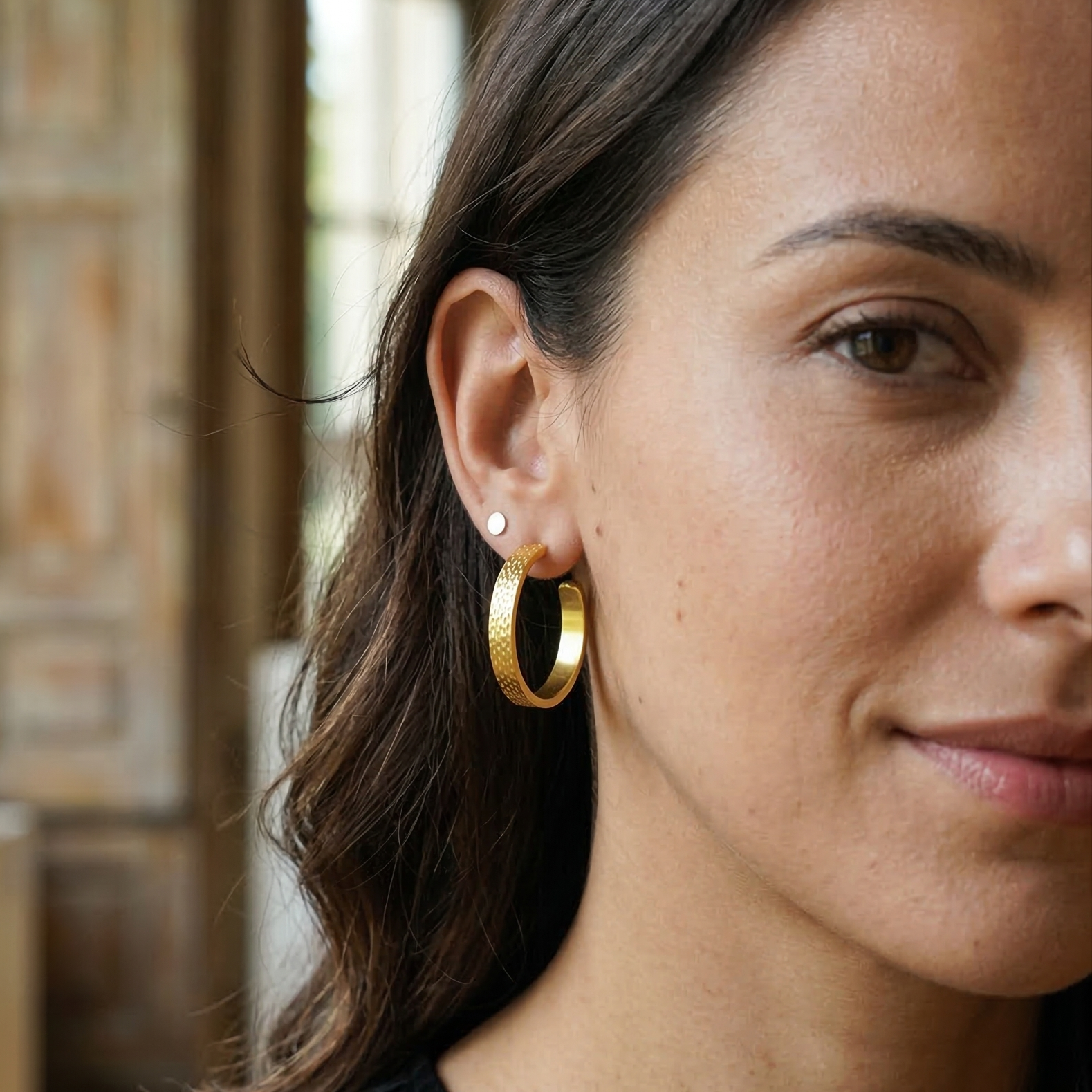 Close-up of a woman wearing gold hoop earrings with a blurred background