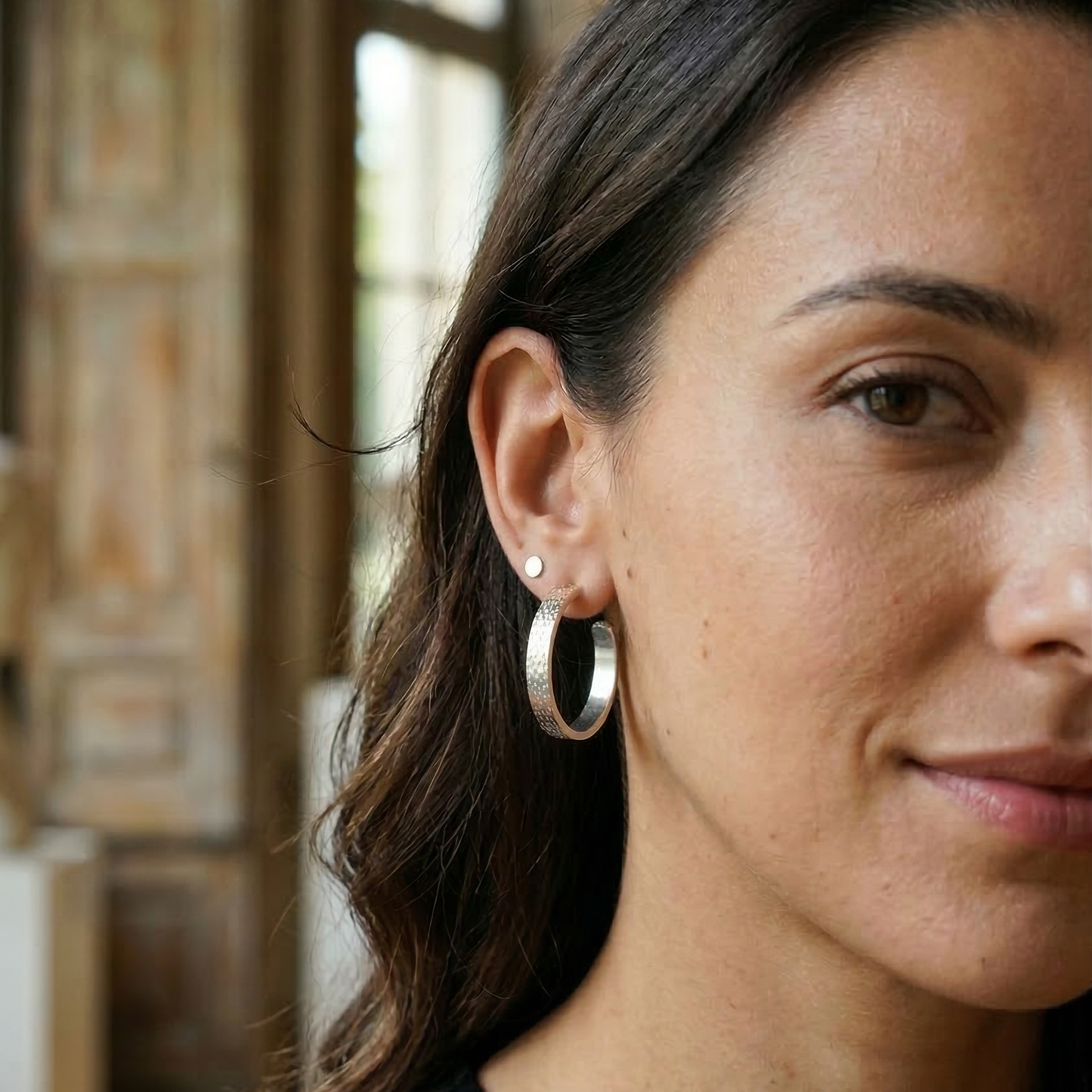 Close-up of a woman wearing silver hoop earrings with a blurred background
