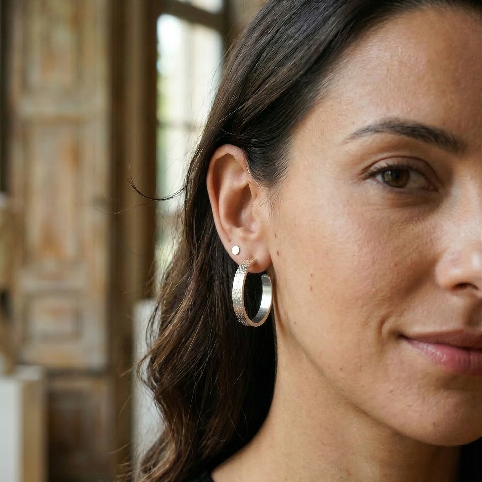 Close-up of a woman wearing silver hoop earrings with a blurred background