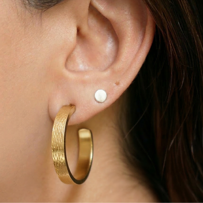 Close-up of an ear wearing a gold hoop earring and a small round earring.