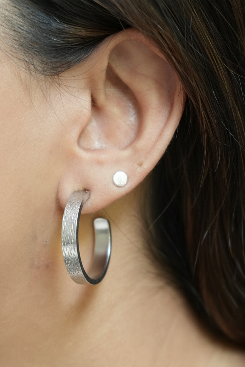 Close-up of an ear wearing a silver hoop earring with a small stud.