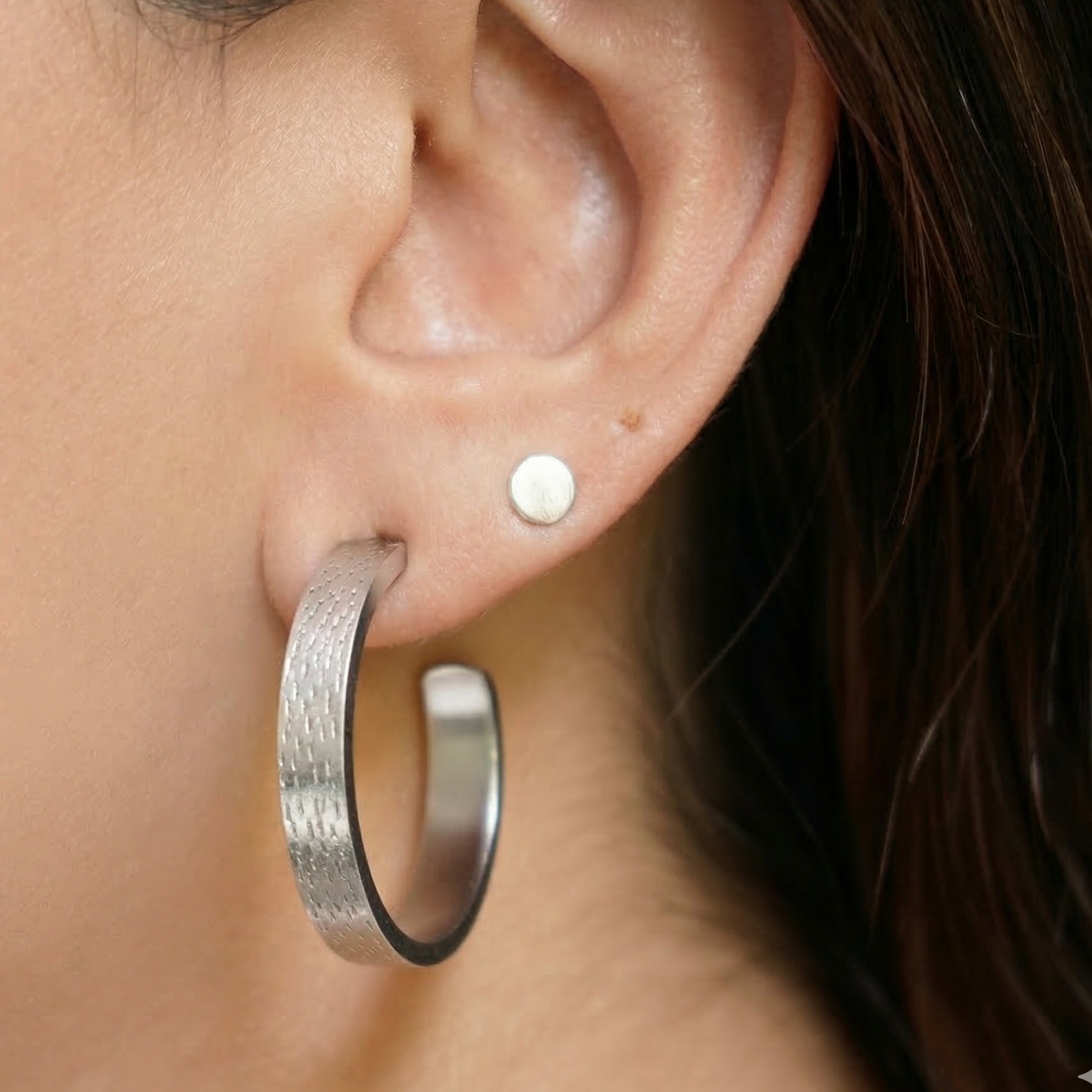 Close-up of an ear wearing a silver hoop earring and a small stud.