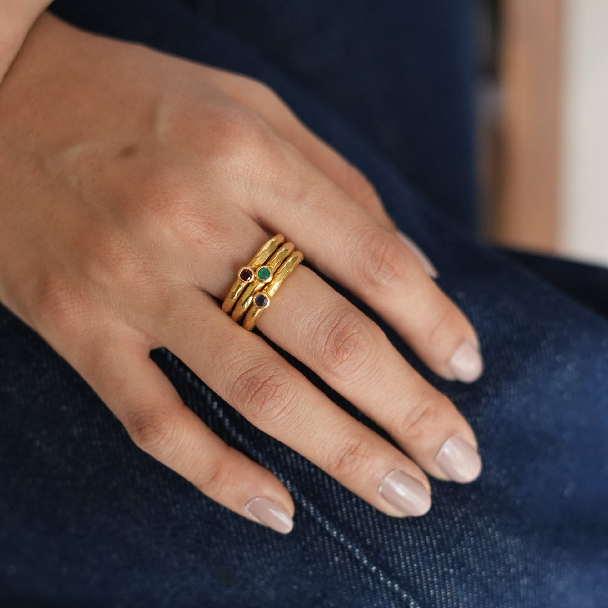 A close-up image of a person's hand wearing a stack of gold-plated silver rings with a textured design.