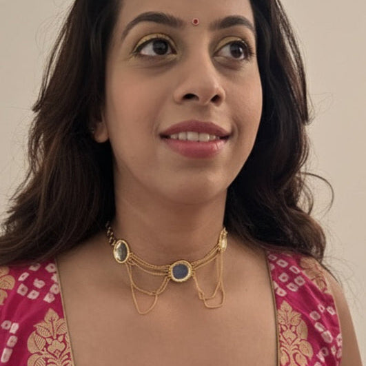 Woman wearing a pink and gold patterned top with gold jewelry against a plain background