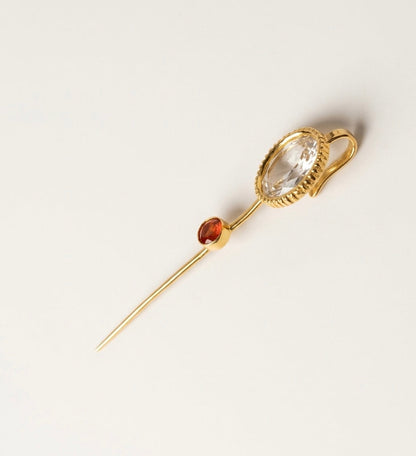Gold earpin with a clear gemstone and carnelian stone on a light gray background