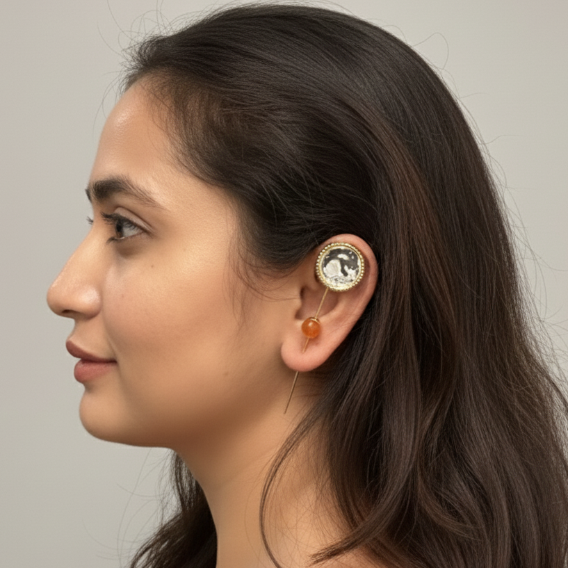 Woman wearing a gold earring with a gemstone on a plain background