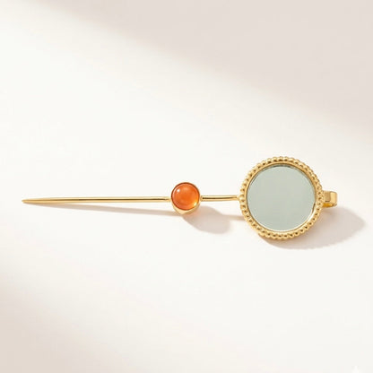 Gold earpin with a clear gemstone and carnelian stone on a light gray background