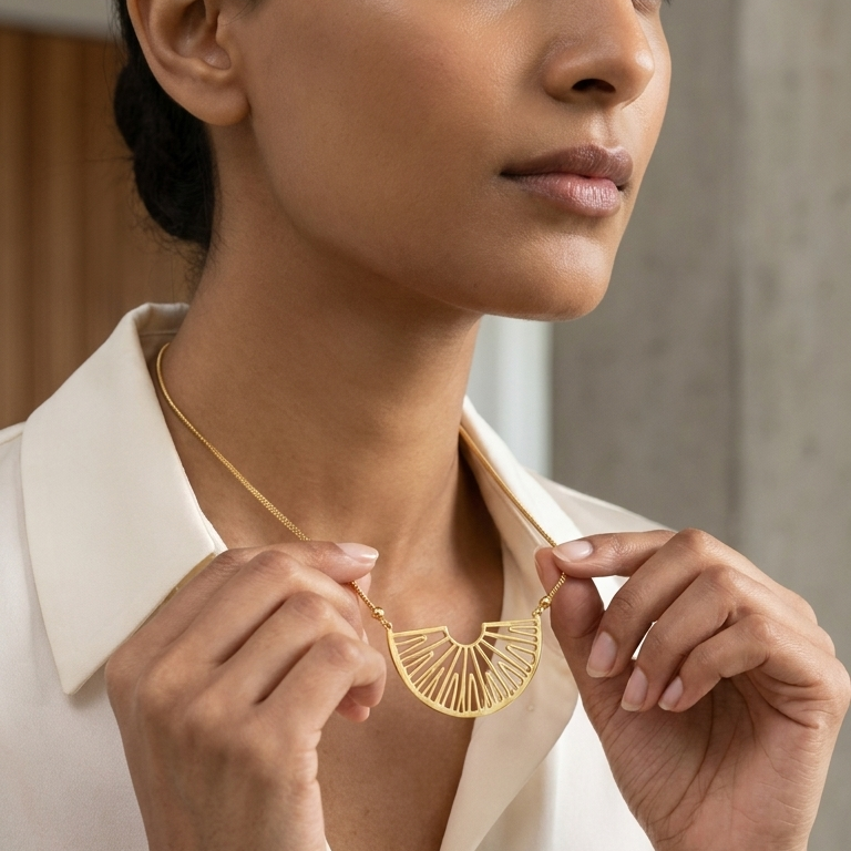 A woman wearing a gold geometric fan-shaped pendant necklace, holding the pendant with both hands against a soft-focus indoor background.