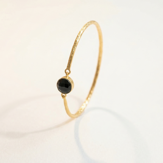 Gold bracelet with a black spinyl  gemstone on a light background