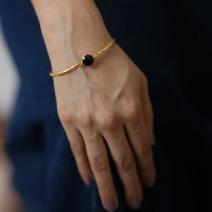 Gold bracelet with a black spinyl stone on a wrist against a dark background