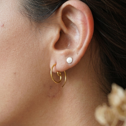 Close-up of an ear wearing gold hoop earrings with a pearl stud.