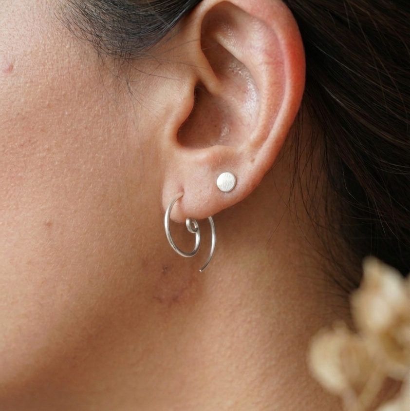 Close-up of an ear wearing a small round earring and a silver hoop earring.
