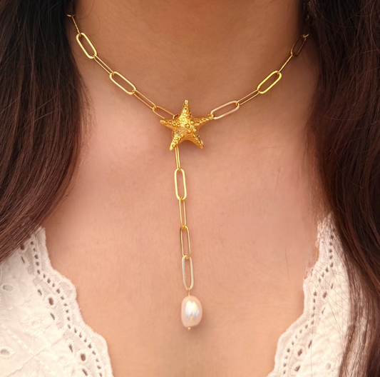 Close-up of a person wearing a gold necklace with a star and pearl pendant.
