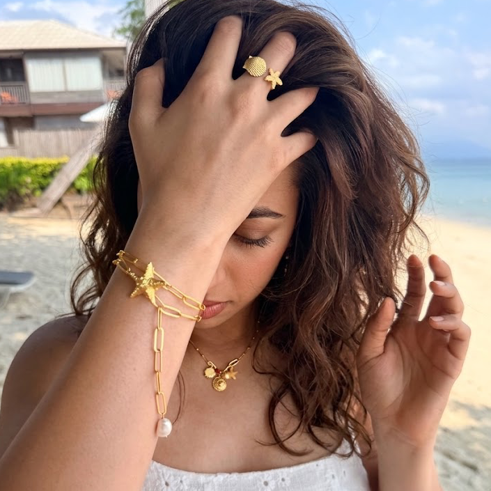 Gold necklace with a starfish pendant and freshwater pearl on a sandy background