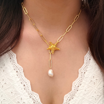 Gold necklace with a star and pearl pendant worn by a person with long dark hair.