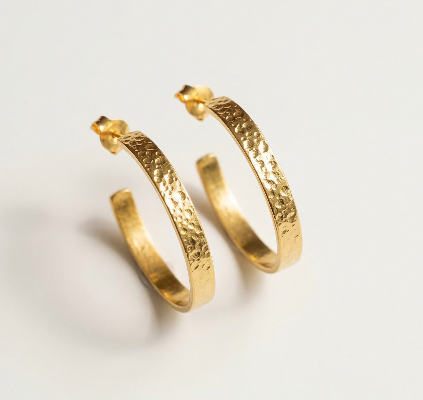 Gold hoop earrings with a textured finish on a light gray background
