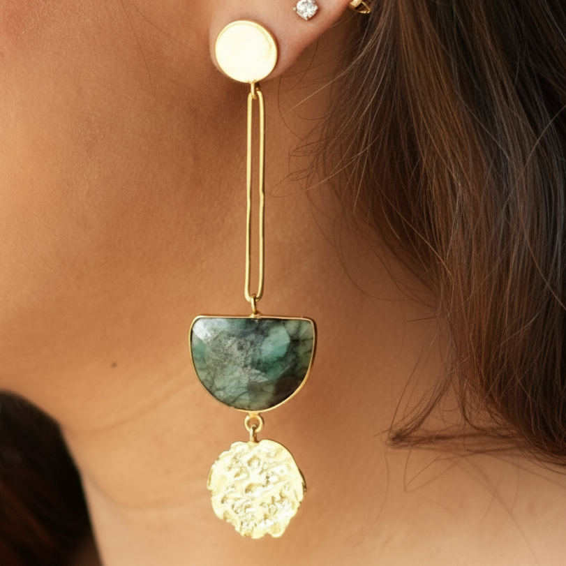 Close-up of an ear with gold earrings featuring a green stone and floral design.
