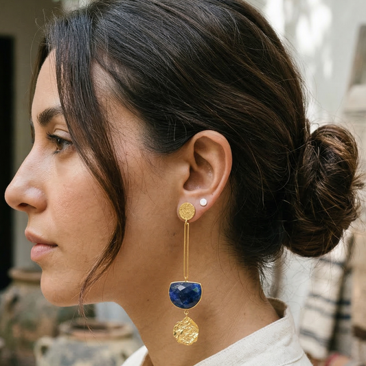 Woman wearing a blue sodolite and gold earring with a blurred outdoor background