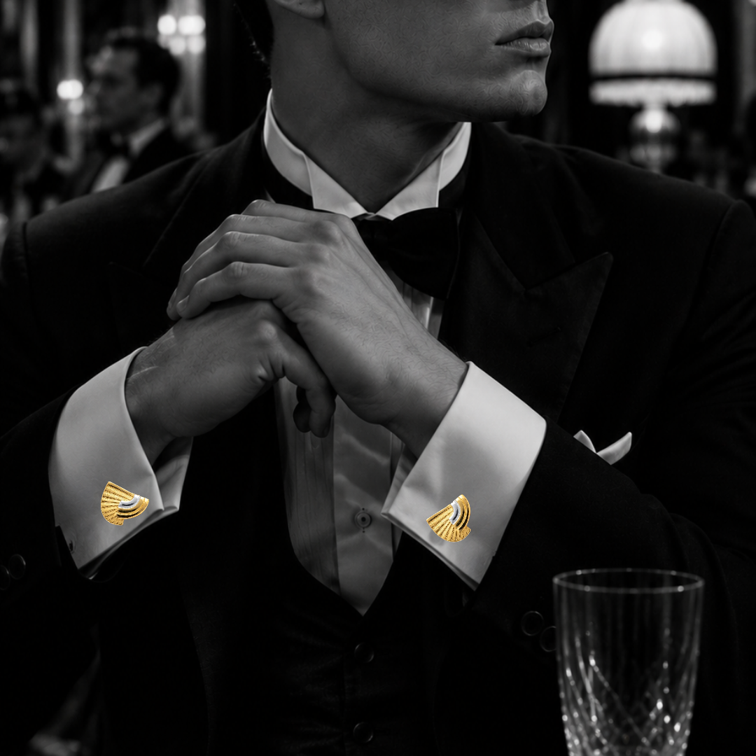 A man in a black tuxedo jacket and bow tie wearing gold cufflinks with a stylized bird design, shown in a black and white photograph with a blurred elegant interior background.