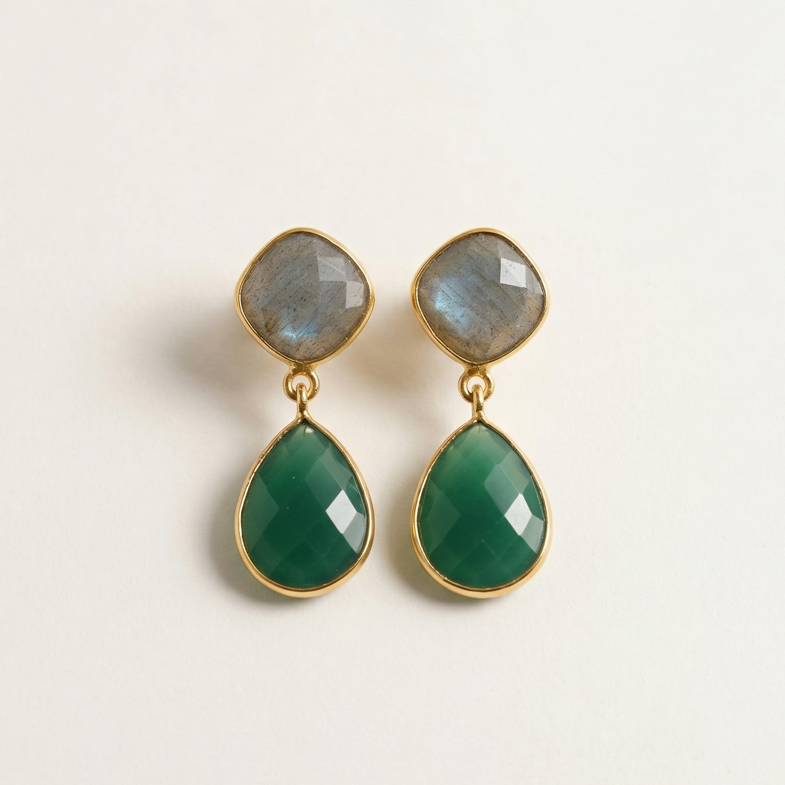 Pair of green teardrop earrings with gold accents on a light beige background